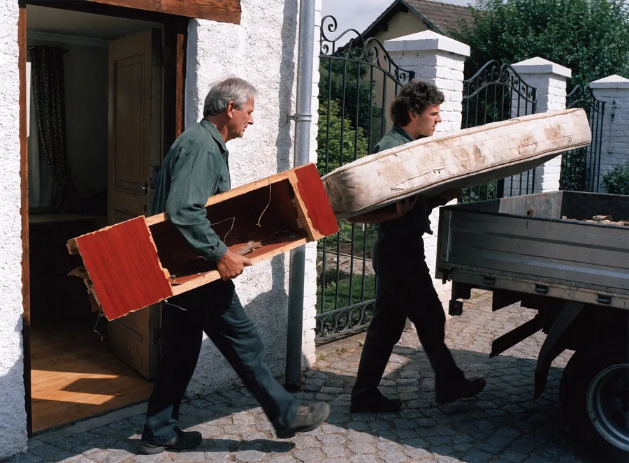 Mitarbeiter tragen Sperrmüll – Matratze und Schrank – aus dem Haus