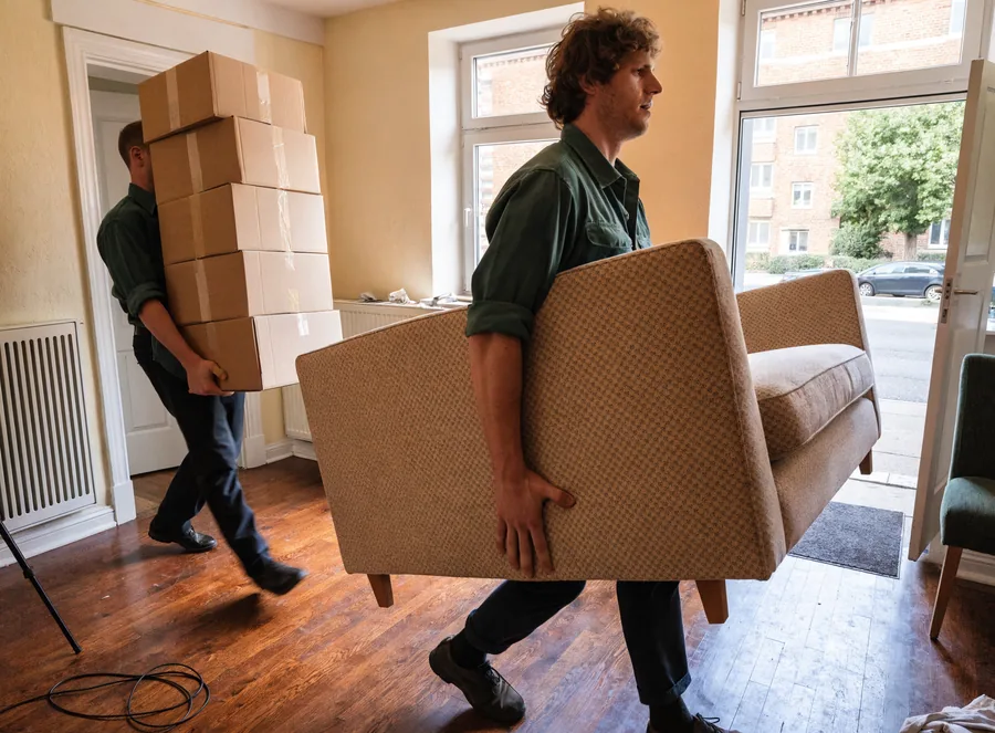 Zwei Mitarbeiter tragen Sofa und Kartons aus einer Wohnung in Essen